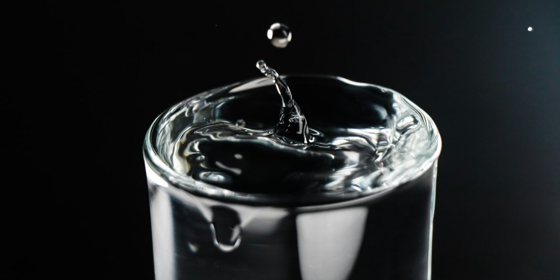 a glass of water with a drop of water falling into it