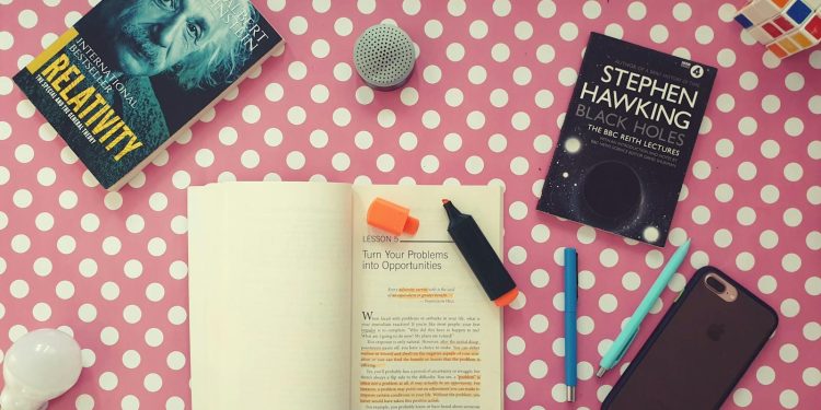 Flat lay of books, stationery, and gadgets on a polka dot desk for a vibrant study setup.