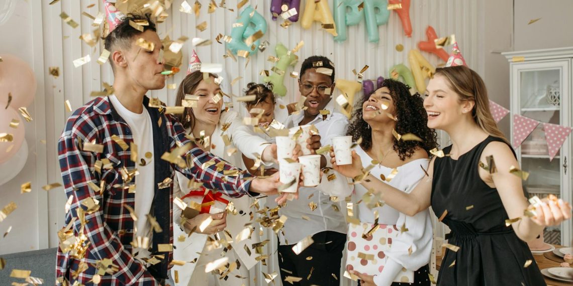A lively indoor birthday party with friends celebrating with confetti and drinks in a decorated room.